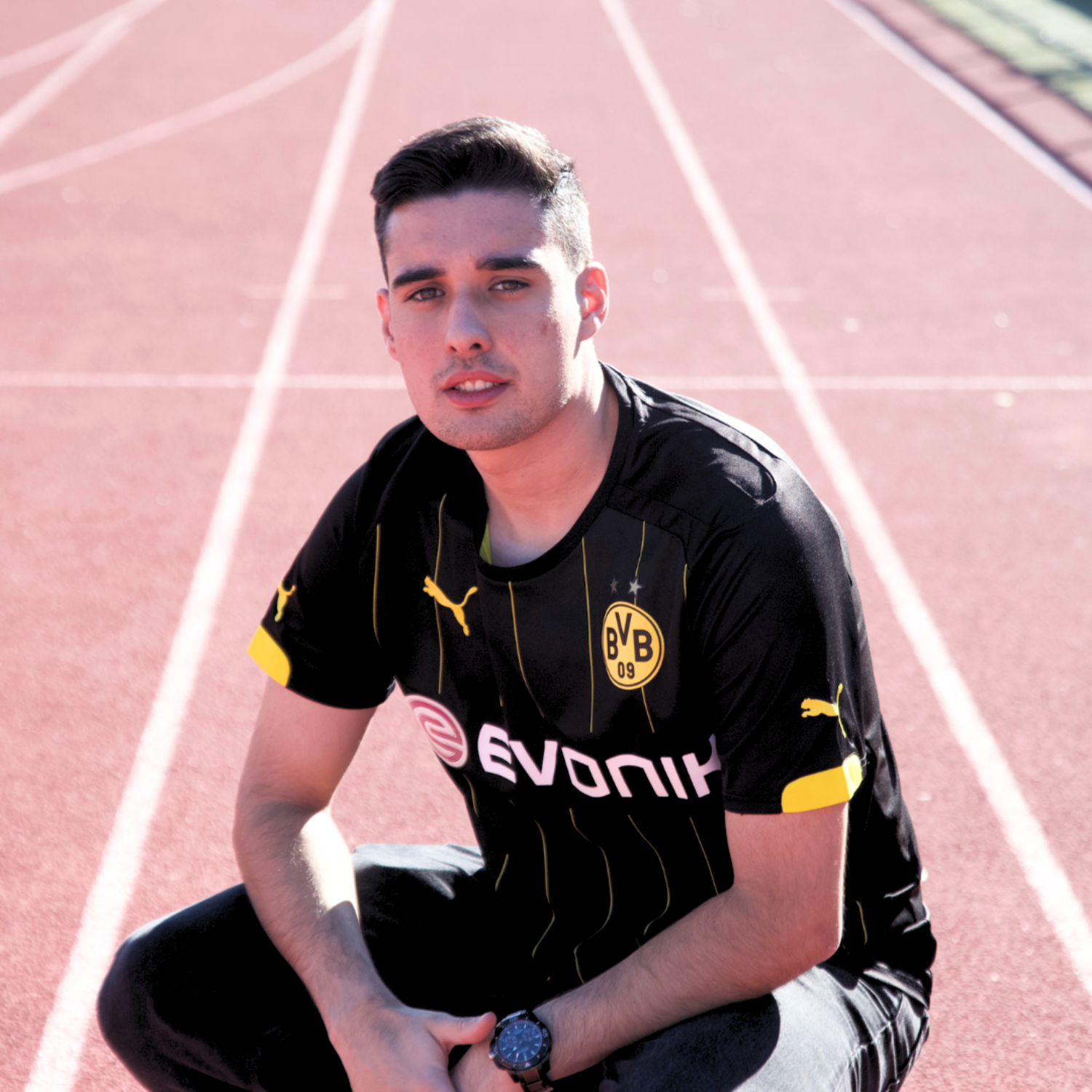 Hombre posando con la camiseta del Borussia Dortmund, agachado en una pista de atletismo. 